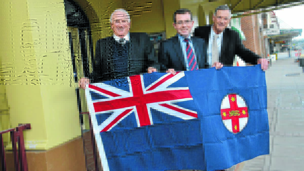 o  Unfurling the flag: Australia Day committee member Malcolm Schumacher, member for Northern Tablelands Adam Marshall and Glen Innes Severn mayor Colin Price with the committee’s new state flag, which will be proudly flying next January 26.