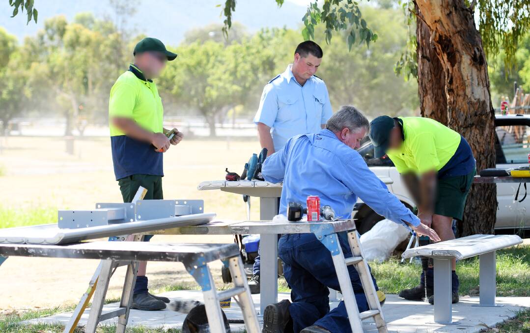 HELPING HANDS: Harrison Fittler looks on and builder Guy McIntosh gives guidance as inmates install a picnic table and benches on their slab. Photo: Gareth Gardner 110119GGA05